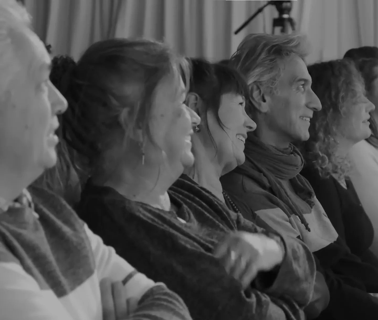 Rij publiek die glimlachend en ontspannen naar het podium kijkt.